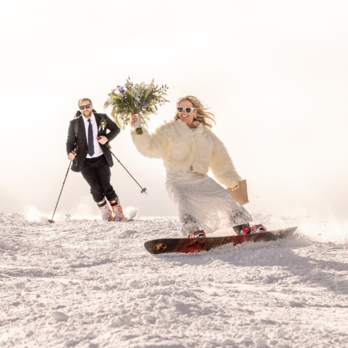 Hochzeit feiern in den Bergen am Arlberg – die schönste Hochzeitslocation für Brautpaare im Winter im Skigebiet – Brautpaar auf Snowboard und Skiern